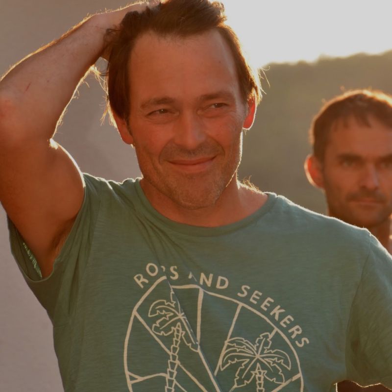 Porträtfoto von einem Mann mit  kurzen braunen haaren und einem olivgrünem T-Shirt mit Sujet von Palmen