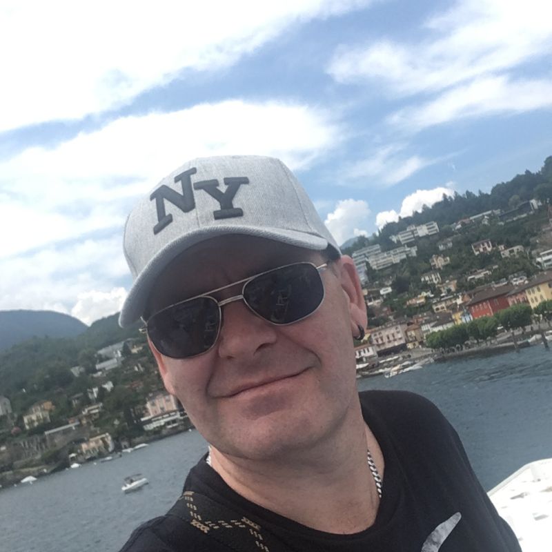 Mann mit Kappe und Sonnenbrille steht an einem Ferienort und macht ein Foto von sich