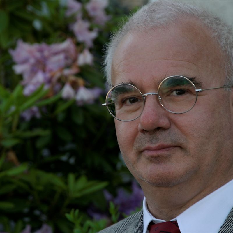 Porträtfoto älterer Mann mit weissen kurzen Harren und runder Brille im Anzug mit Kravatte