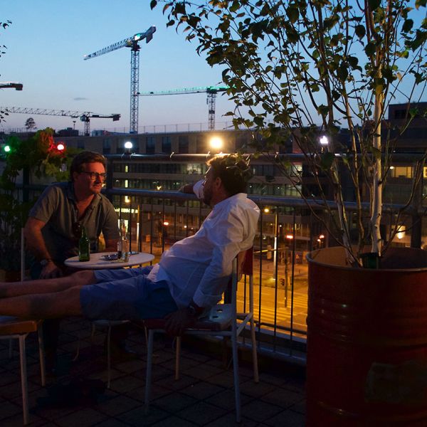 Zwei Männer sitzen auf Dachterrasse und unterhalten sich bei einem Bier und lassen den Tag ausklingen