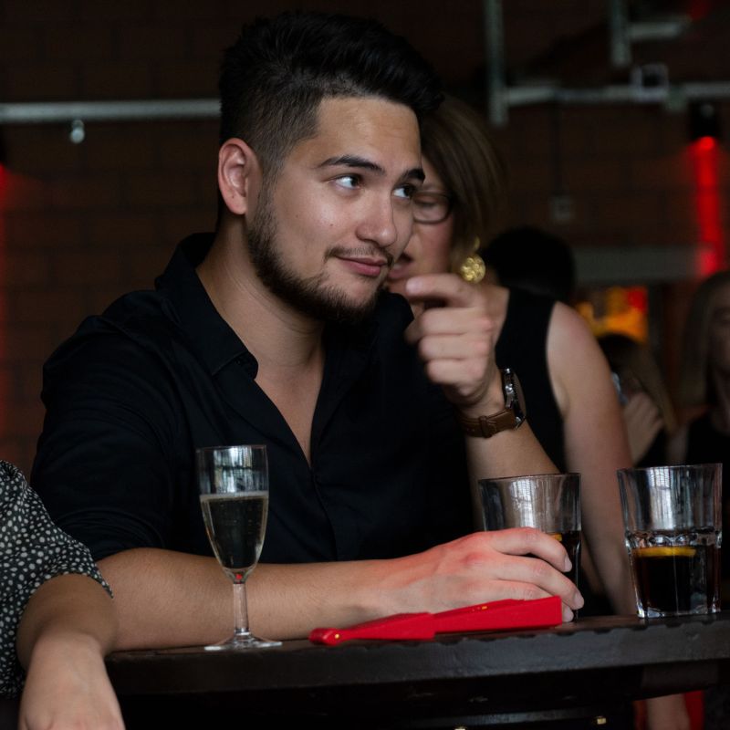 Mann mit schwarzem Hemd welcher an einer Bar ein Glas Cola trinkt