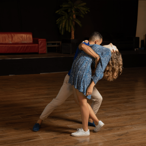 Mann hält eine Frau im blauen gepunkteten Kleid, diese beugt sich nach hinten und lässt ihr Haar fallen.