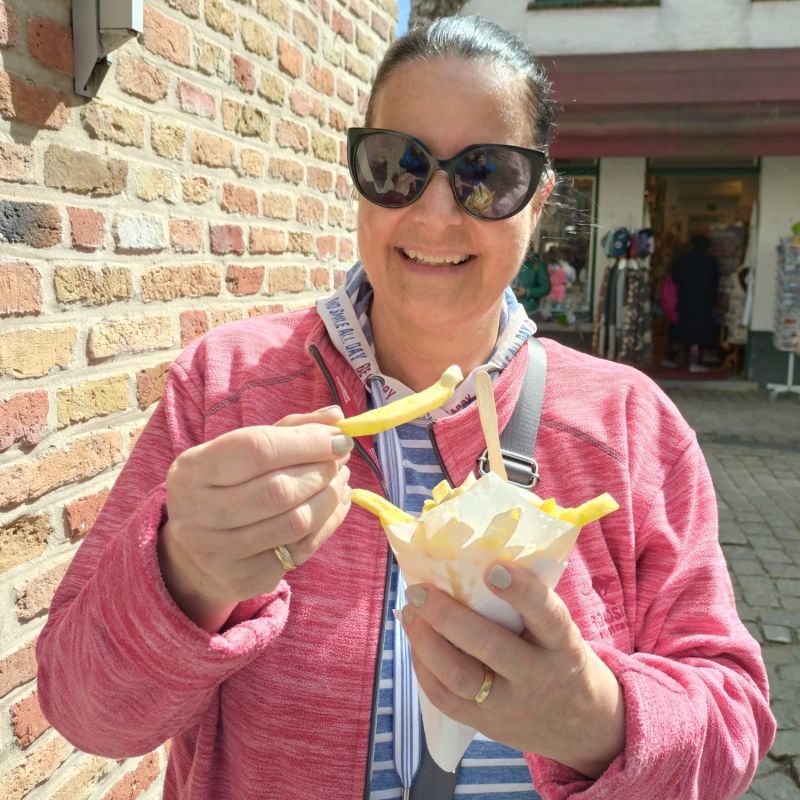 Frau mit Sonnenbrille und roter Jacke am Pommes Frites essen
