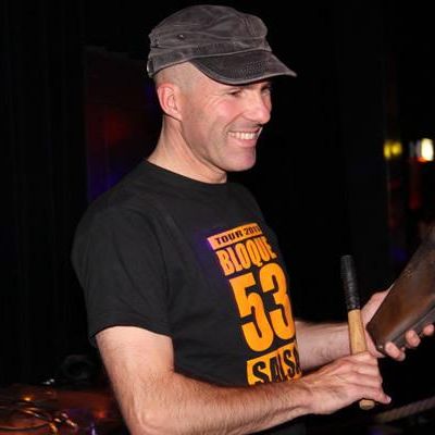 Porträtfoto von einem Mann mit grauem Cap und schwarzen T-Shirt mit oranger Aufschrift