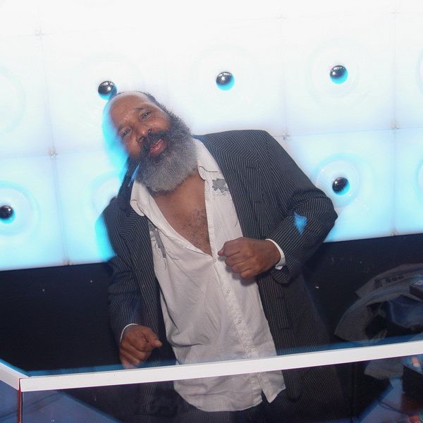 Mann mit grauem  Bart vor einer Wand mit weissen Lampen