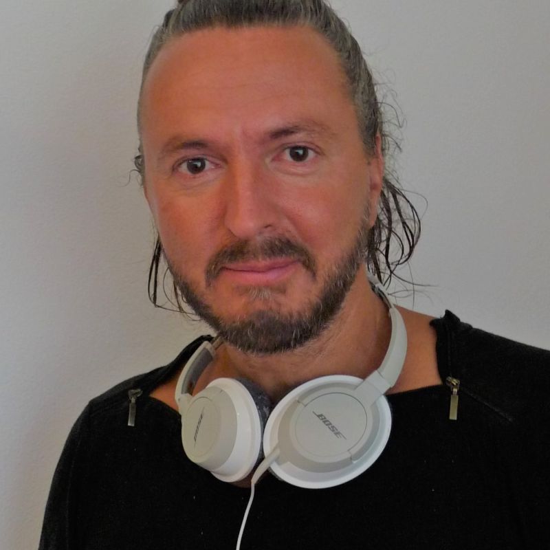 Mann mit langen Haaren und dreitages Bar mit weissen Kopfhörer um den Hals und einem schwarzen T-Shirt