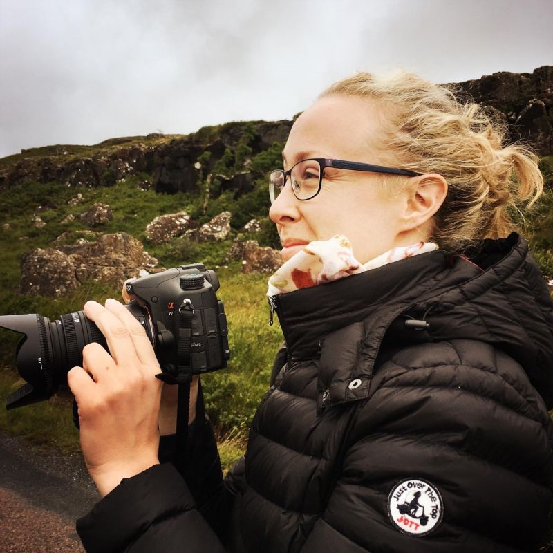 Junge Frau mit blonden Haaren in den Bergen mit einem Fotoapparat
