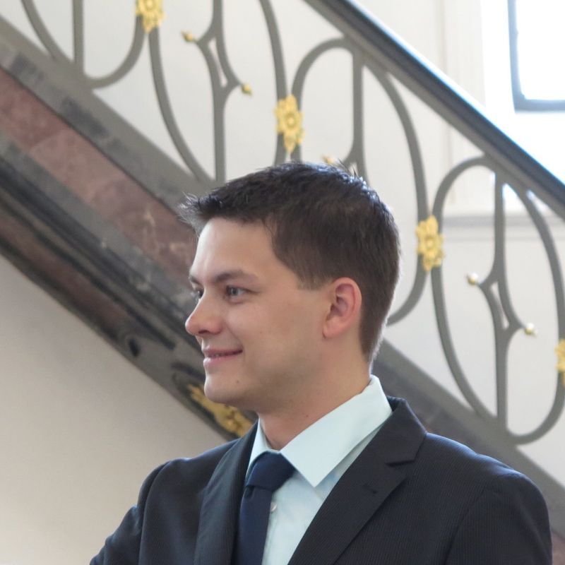 Junger Mann im Anzug mit blauer Krawatte vor einer Treppe aufgenommen