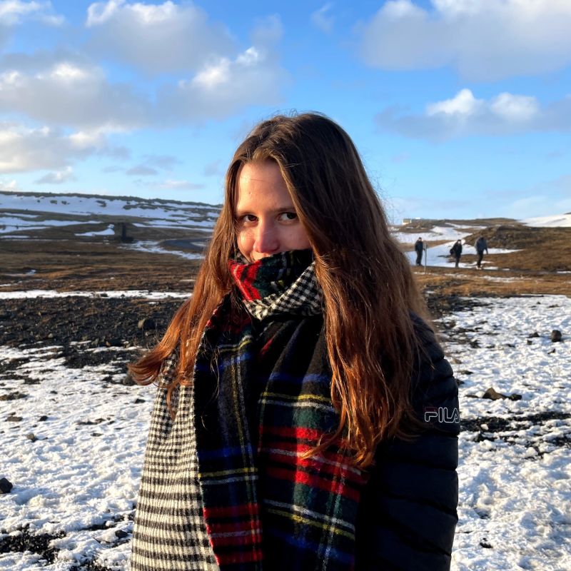 Junge Frau mit langen braunen Haaren und einem Schal vor dem Gesicht auf einem Schneefeld