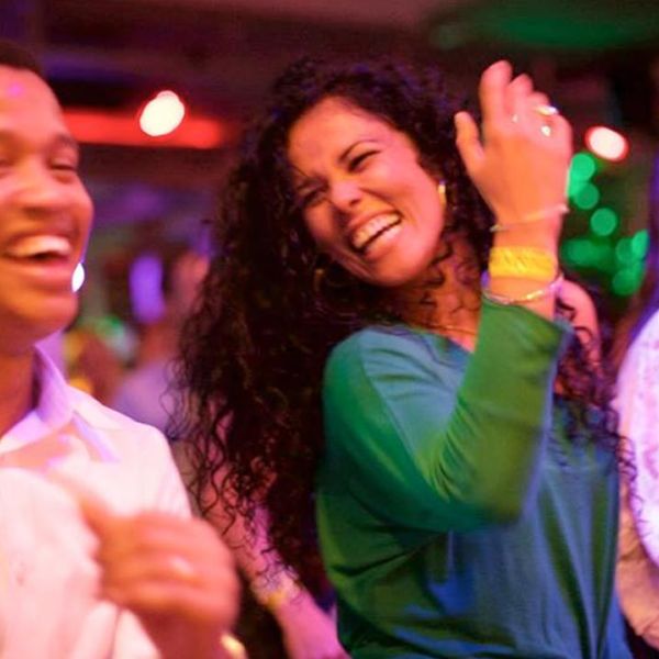 Frau im grünen Klein strahlt und lächelt beim Salsatanzen Mann im weissen Hemd lacht und tanzt neben ihr