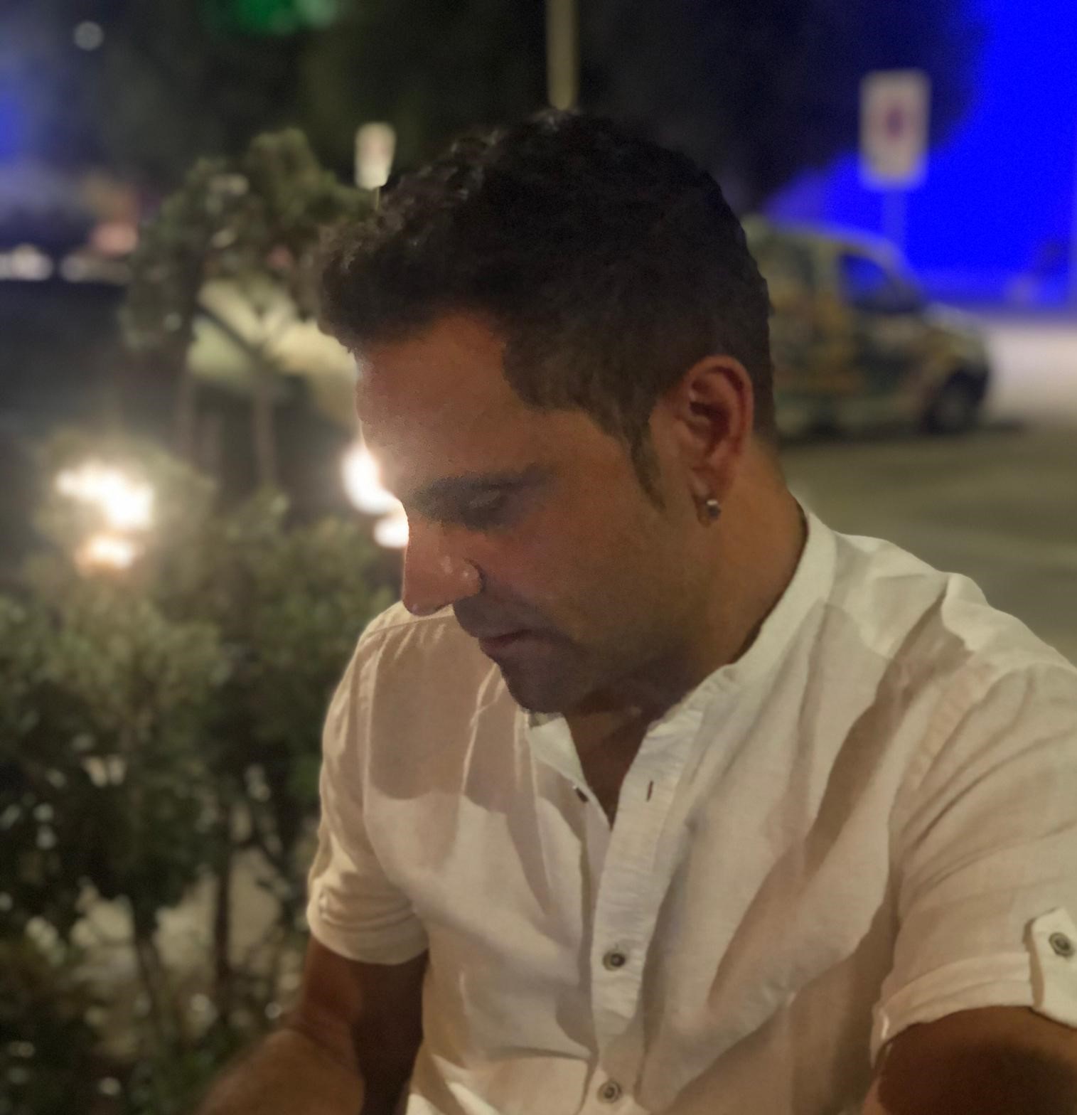 Mann mit weissem kurzarm Hemd welcher nach unten schaut, aufgenommen draussen am Abend