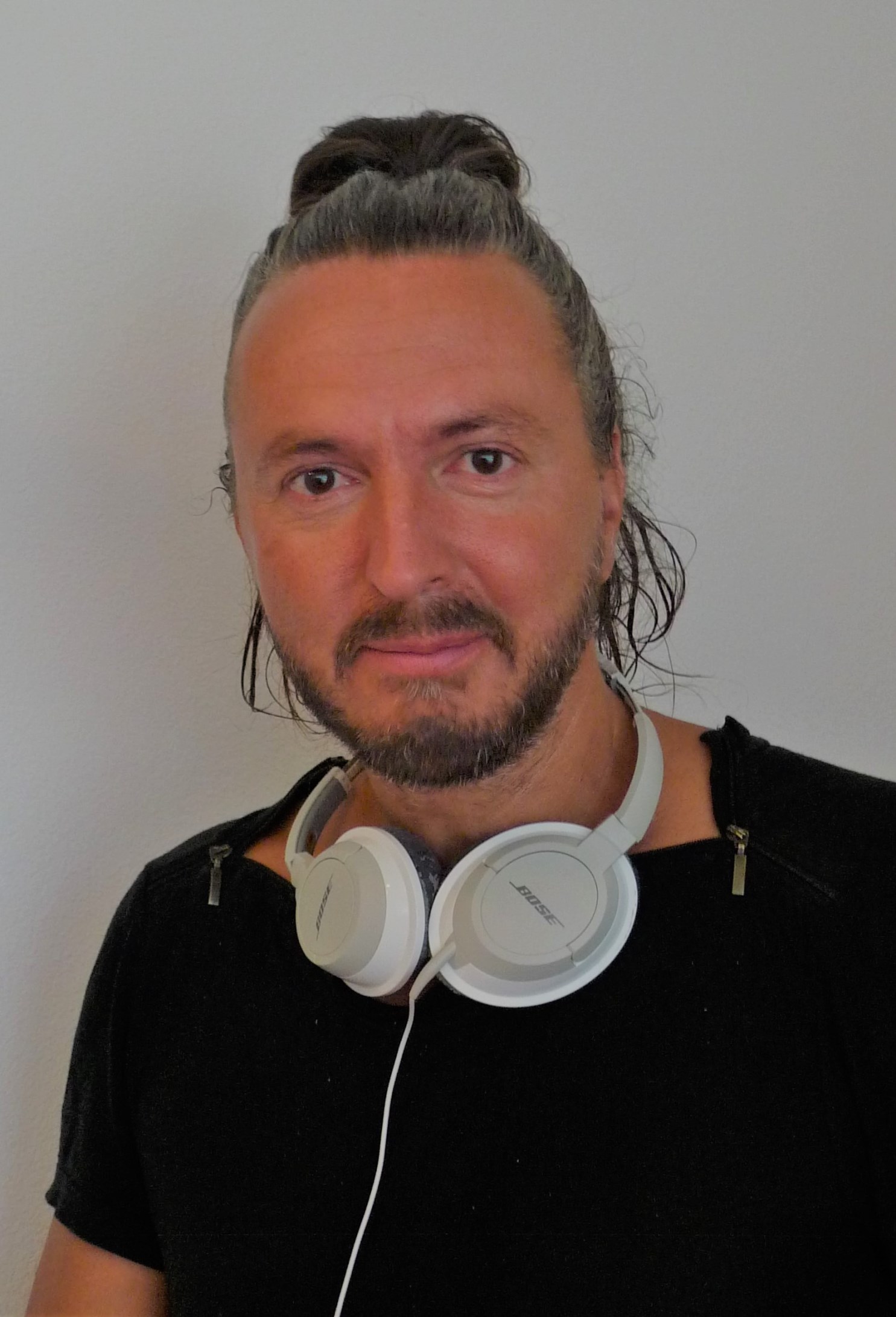 Mann mit langen Haaren und dreitages Bar mit weissen Kopfhörer um den Hals und einem schwarzen T-Shirt