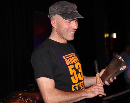 Porträtfoto von einem Mann mit grauem Cap und schwarzen T-Shirt mit oranger Aufschrift