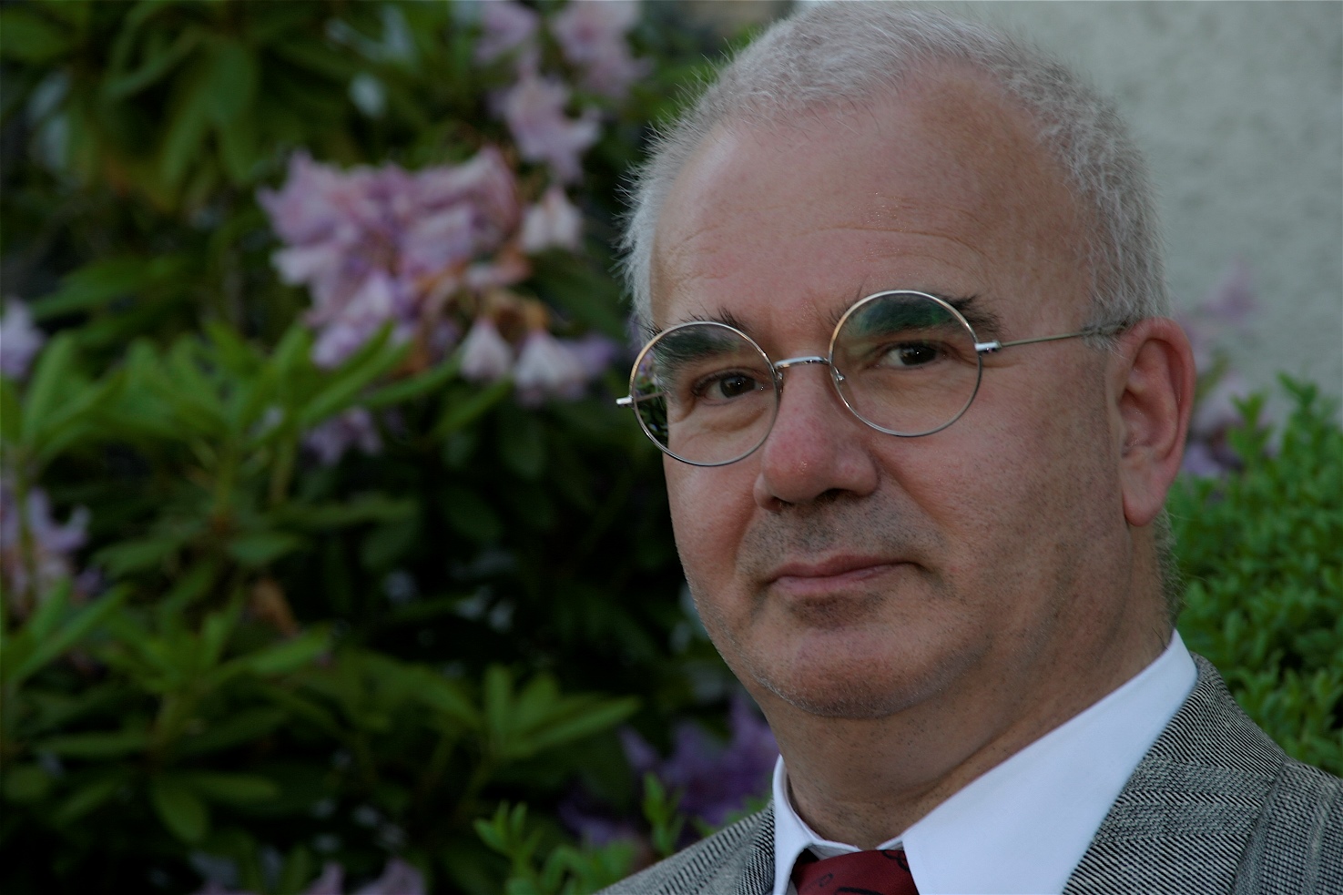 Porträtfoto älterer Mann mit weissen kurzen Harren und runder Brille im Anzug mit Kravatte