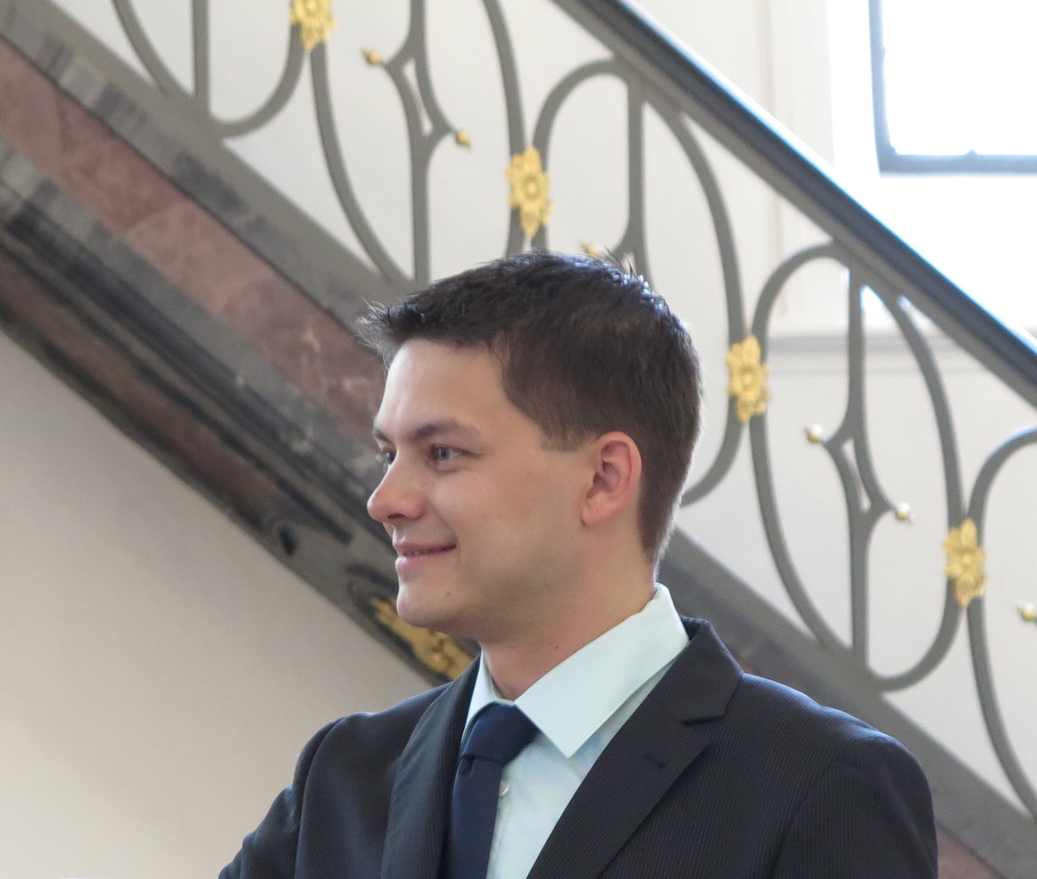 Junger Mann im Anzug mit blauer Krawatte vor einer Treppe aufgenommen