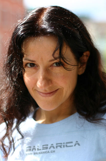 Porträtfoto von einer Frau mit langen lockigen dunklen Haaren, welche ein T-Shirt mit dem Schriftzug SalsaRica trägt