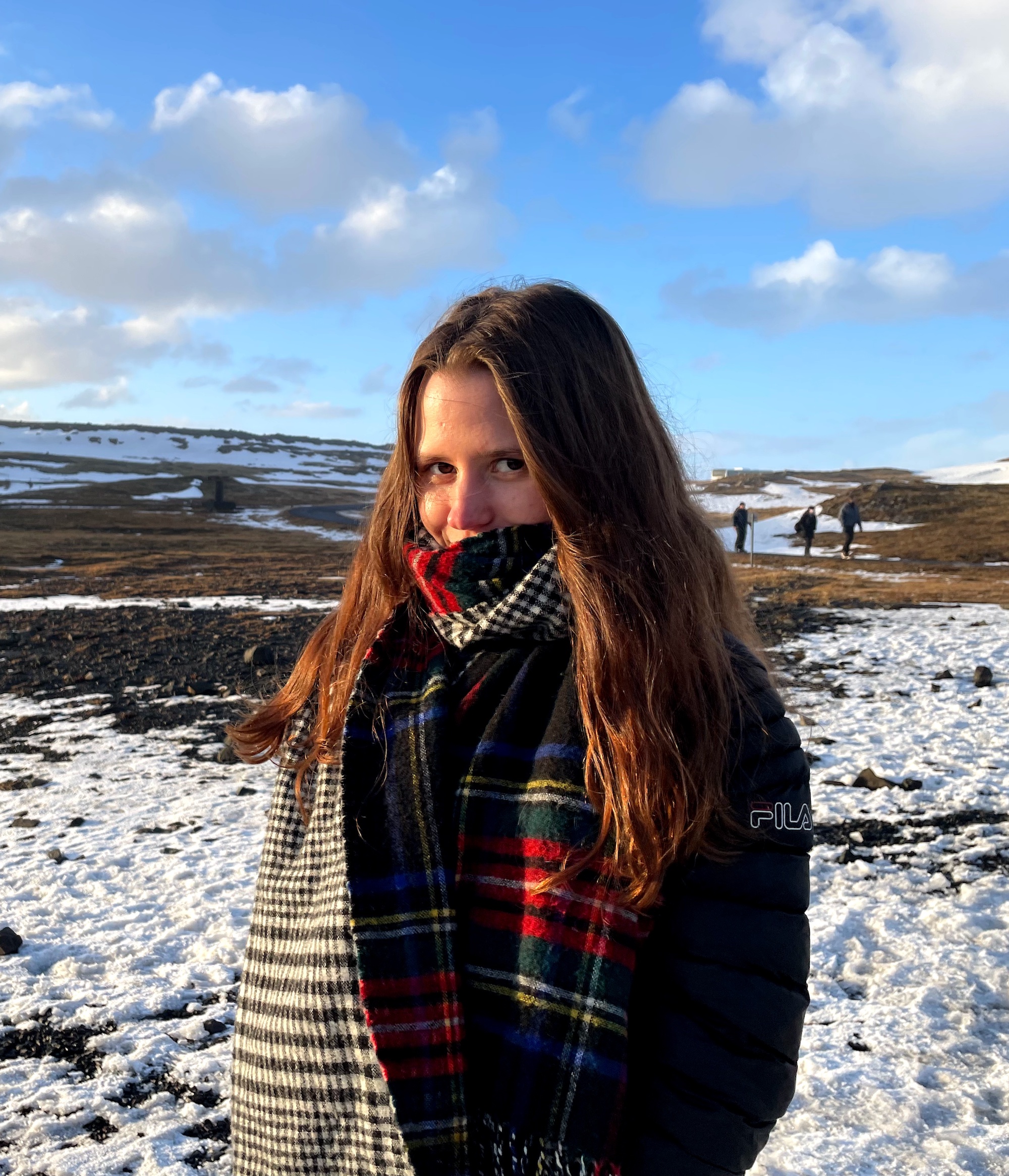 Junge Frau mit langen braunen Haaren und einem Schal vor dem Gesicht auf einem Schneefeld