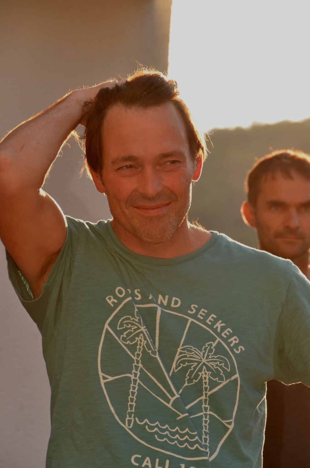 Porträtfoto von einem Mann mit  kurzen braunen haaren und einem olivgrünem T-Shirt mit Sujet von Palmen