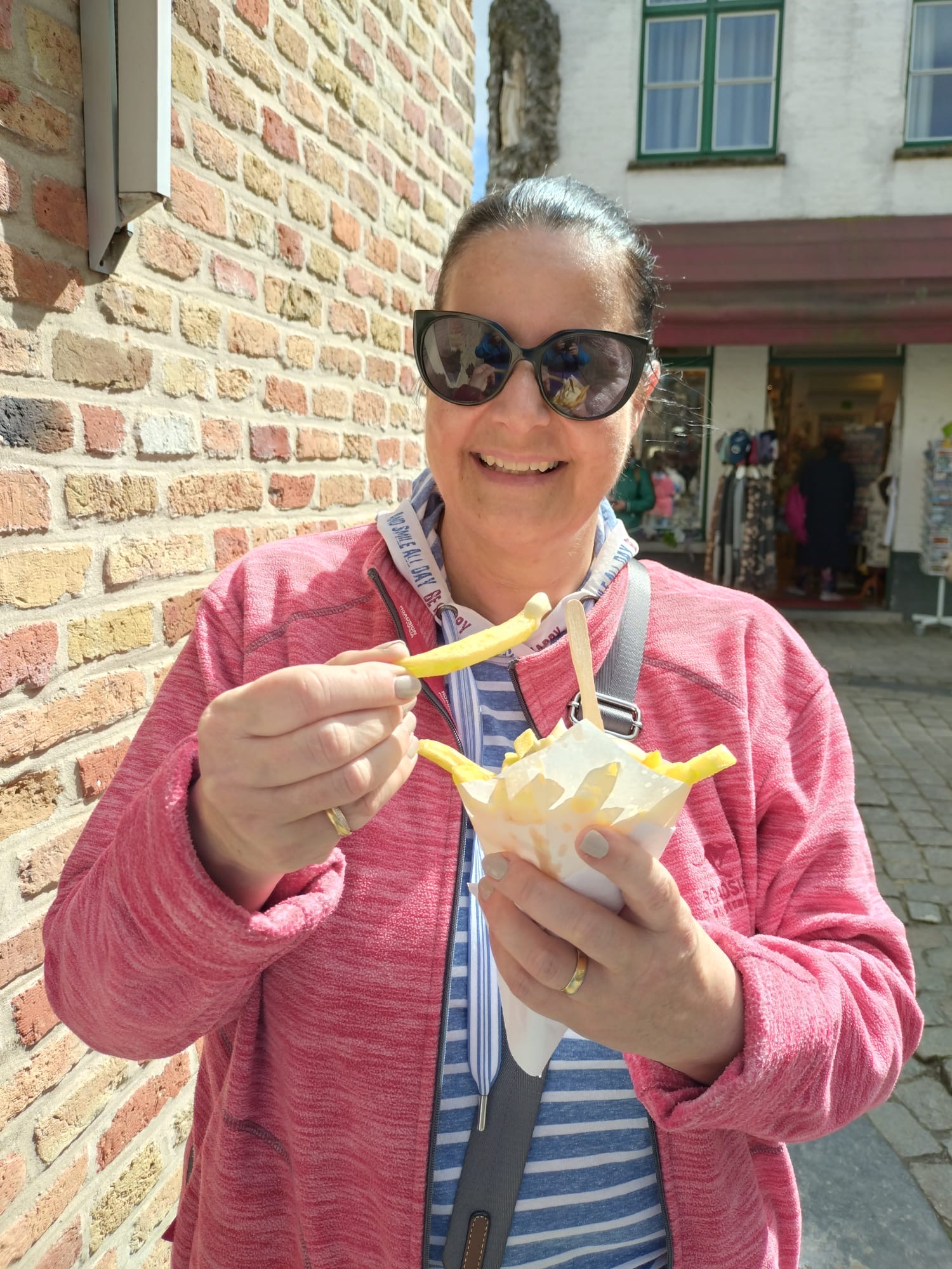 Frau mit Sonnenbrille und roter Jacke am Pommes Frites essen