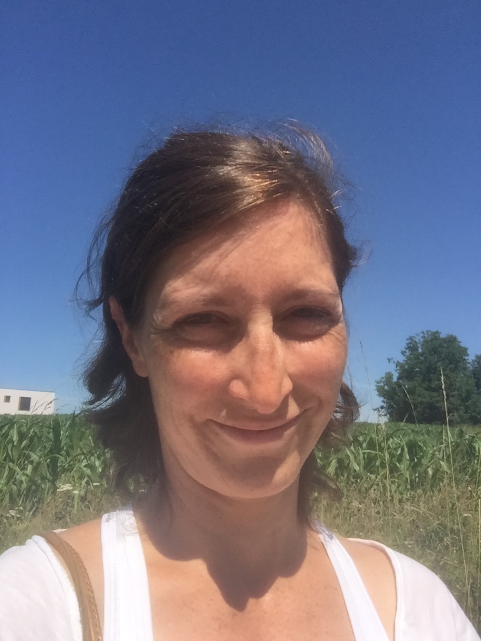 Frau lächelt in die Kamera mit ihren kurzen Haarren. Sie steht auf einer grünen Wiese