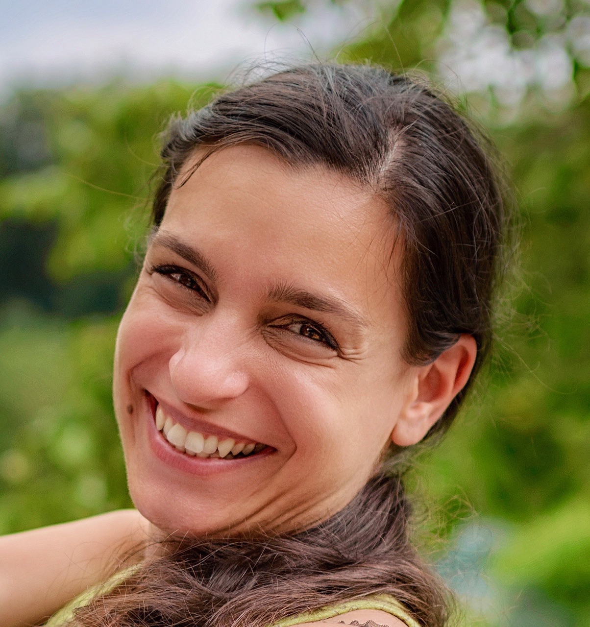 Gesicht von einer stark lachenden Frau mit braunen Haaren steht in der grünen Natur