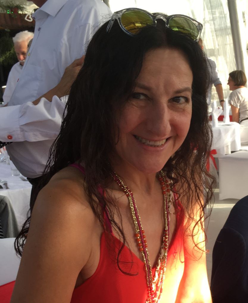 Frau mit langen lockigen braunen Haaren sitzt an einem Tisch und trägt ein rotes Top