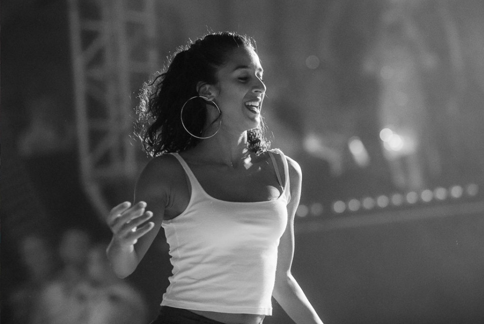 Frau im weissen Top tanzt auf einer Bühne. Sie hat Spass und lächelt