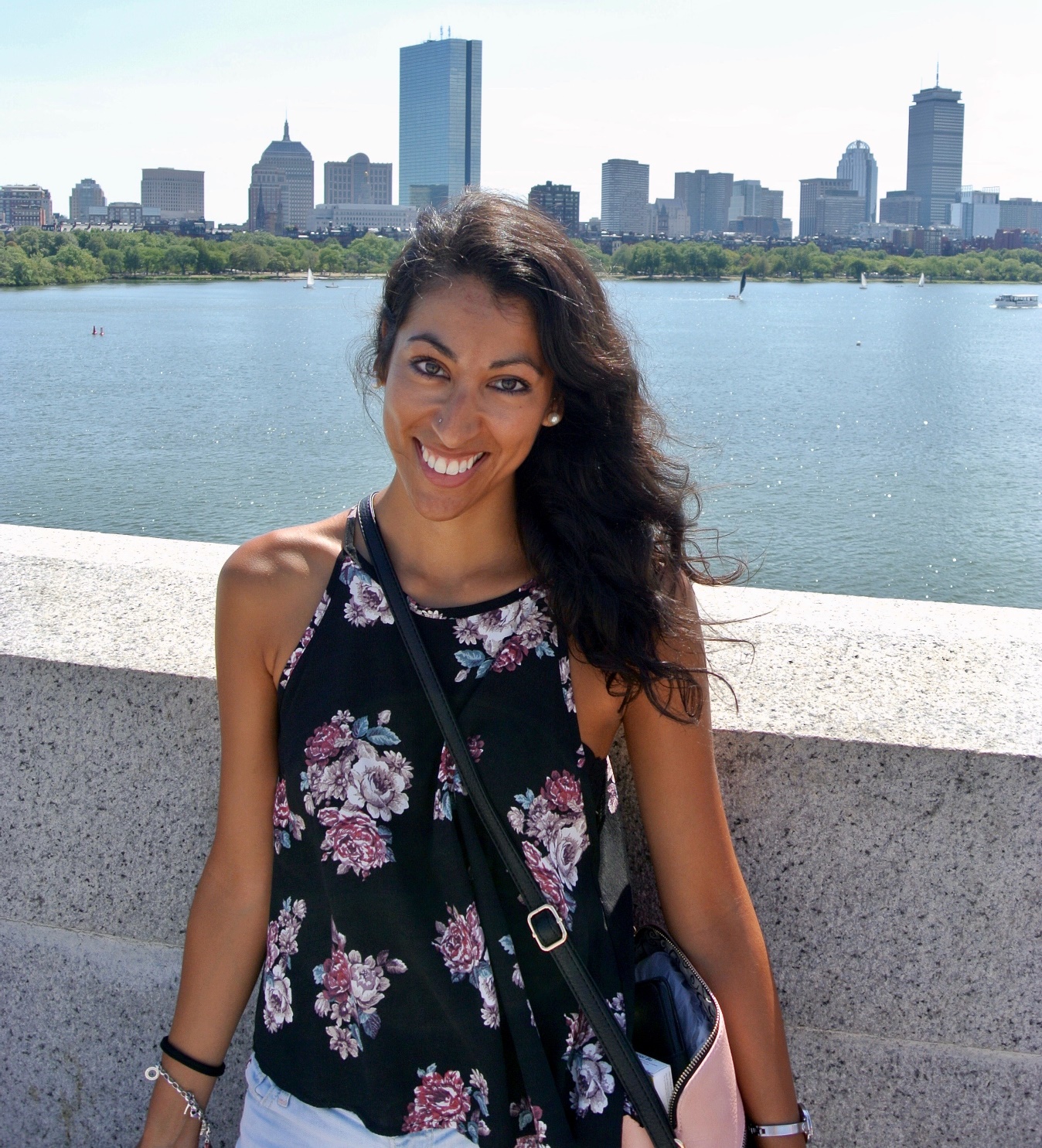 Frau steht am Ufer eines Sees auf einer Brücke und trägt eine sommerliche Bluse, ihr Haar ist vom Wind zerzaust und sie lächelt