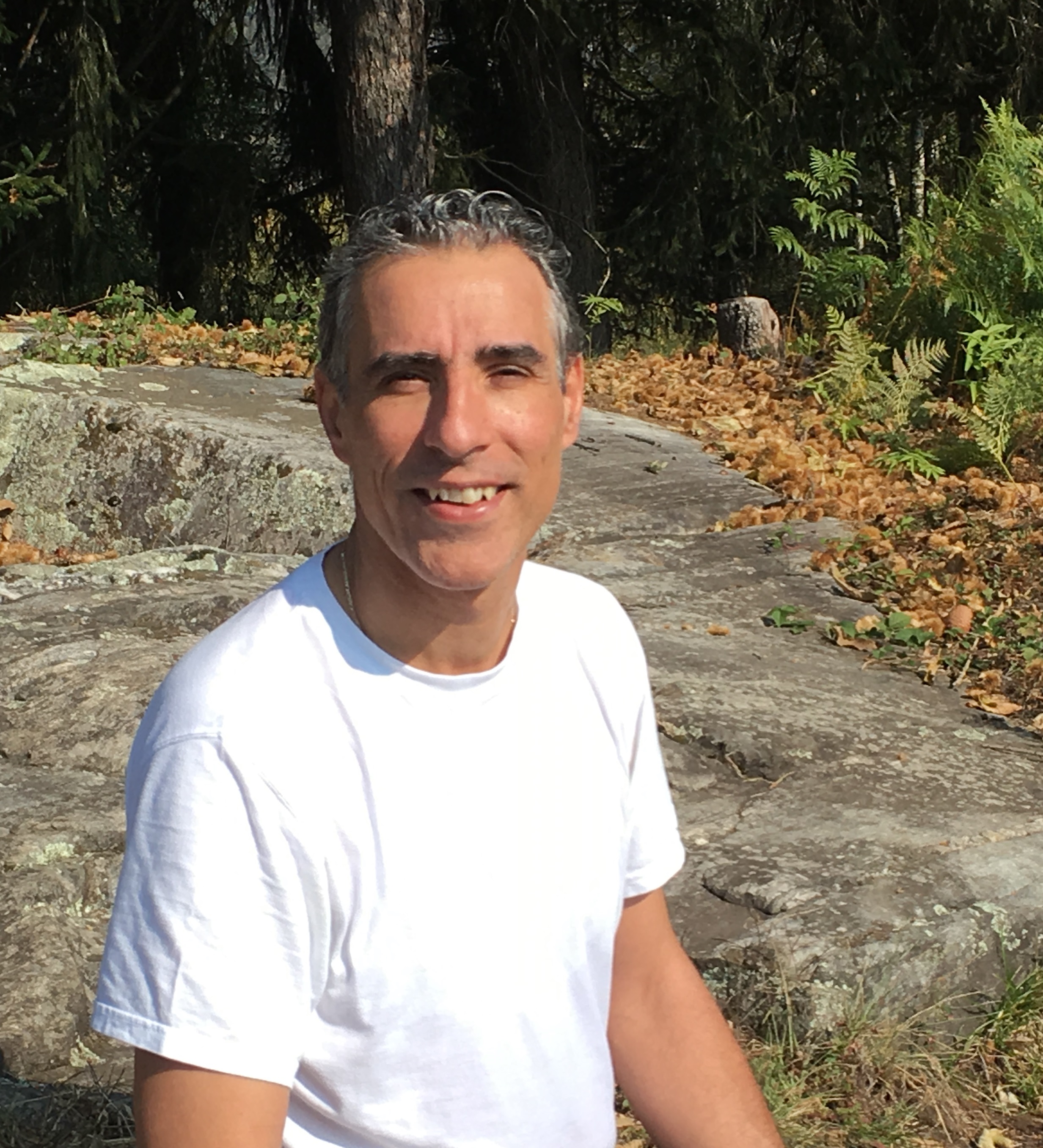 Mann steht im Wald und trägt ein weissen Shirt und lächelt in die Kamera