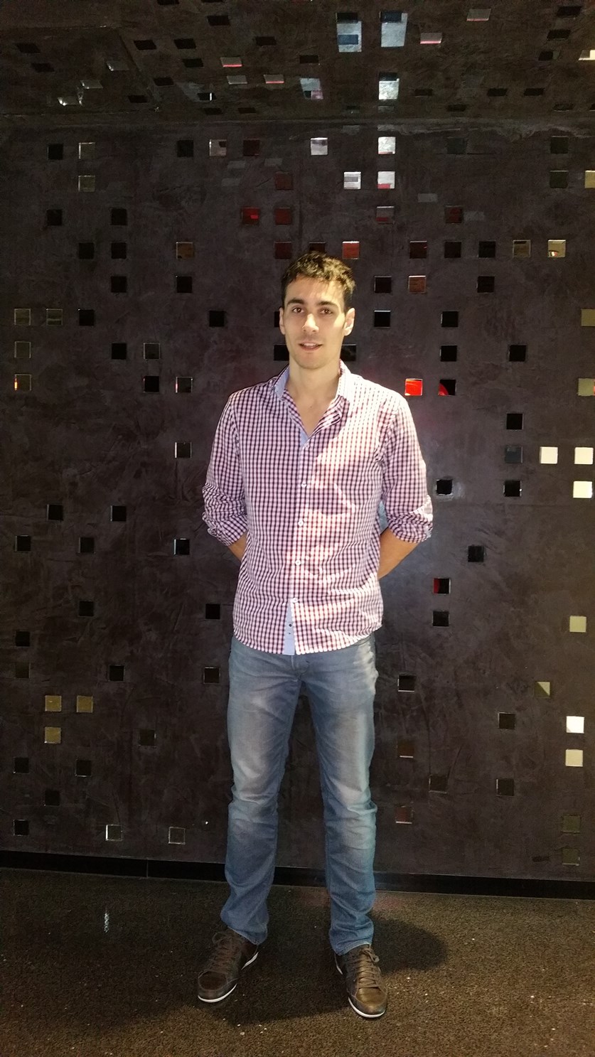 Mann im Karohemd steht vor einer Metallwand und hat die Arme hinter dem Rücken verschränkt