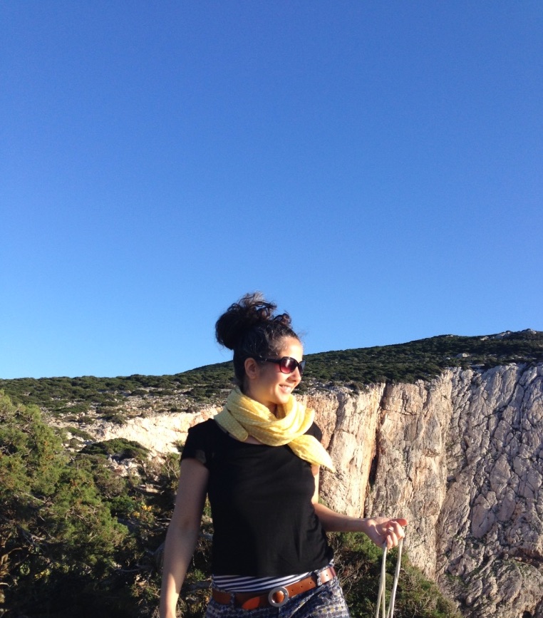 Frau steht vor riesigen Felsen mit tiefem Abgrund und trägt eine Sonnenbrille und einen gelben Schal